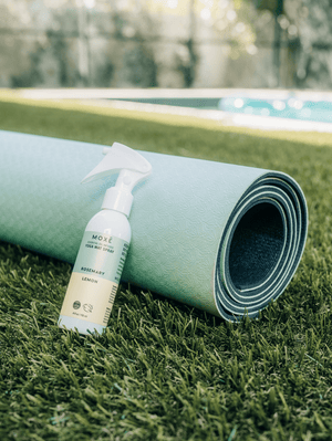 MOXĒ Rosemary Lemon Yoga Mat Spray leaning against green yoga mat